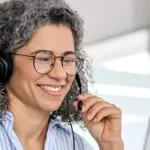 mulher falando por fone portátil e olhando computador