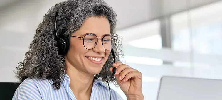 mulher falando por fone portátil e olhando computador