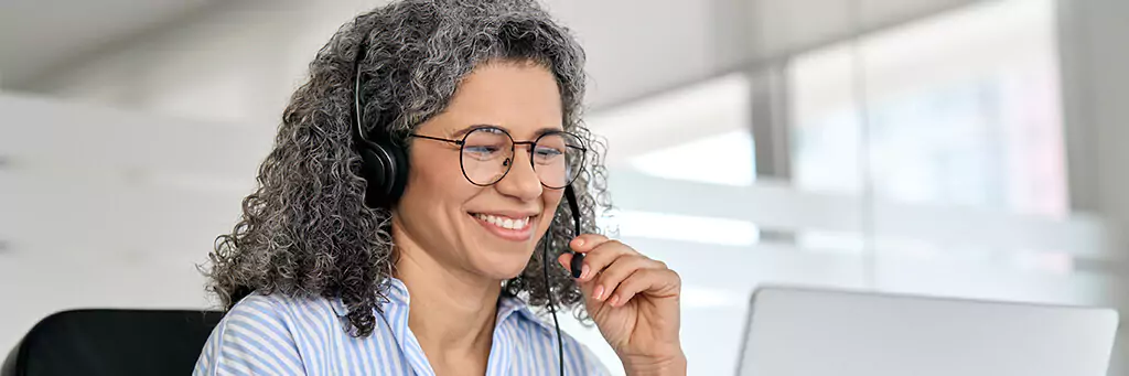 mulher falando por fone portátil e olhando computador