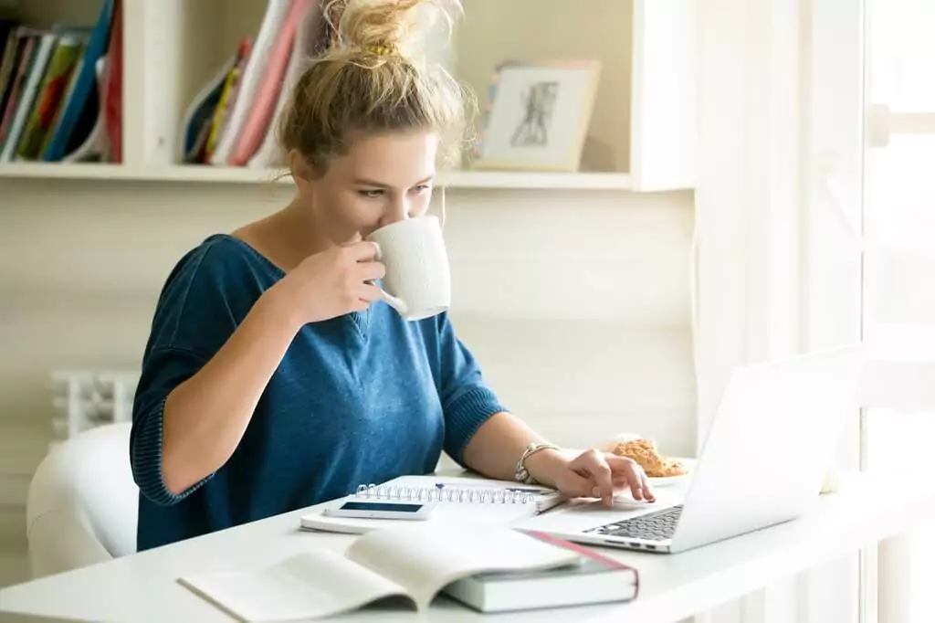 moça tomando bebida e mexendo em computador em escritório